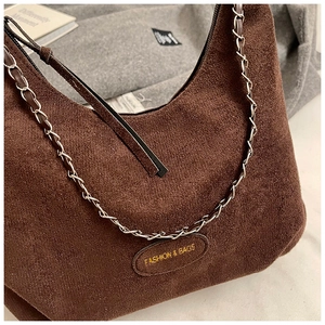 Dettaglio borsa sottobraccio in camoscio marrone con placca logo oro e catena in metallo
