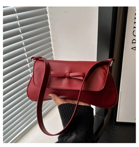 Detail of a deep red matte leather underarm bag with a 3D bow accent and shoulder strap