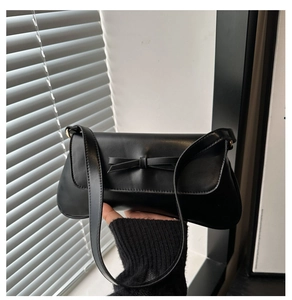 Detail of minimalist black PU leather underarm bag with decorative bow and flap closure