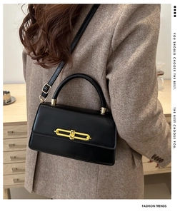 Detail of black leather crossbody bag featuring gold chain lock and adjustable strap