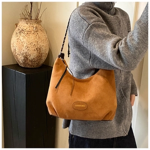 Dettaglio della borsa hobo in camoscio caramello con targhetta e tracolla in catena