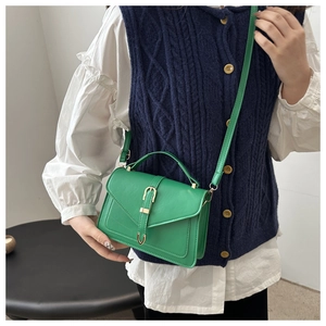 Person wearing bright green leather envelope bag with adjustable strap and metal clasp