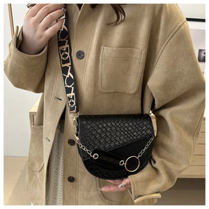 Détail du sac selle noir avec texture tressée, chaîne dorée et bandoulière à motifs