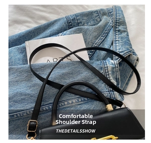 Detail of matte black leather bag featuring a gold J-shaped metal buckle and slim strap