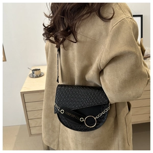 Détail du rabat à texture tressée et de l'anneau doré sur le sac bandoulière noir