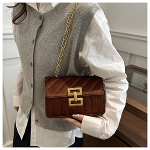 Detail van een bruine fluwelen crossbodytas met ketting gedragen door een model