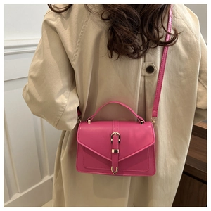 Detail of pink crossbody bag with gold horseshoe buckle worn with a beige trench coat
