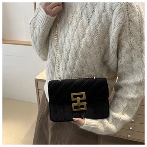 Detail of black velvet crossbody bag with gold chain strap and square lock on grey sweater
