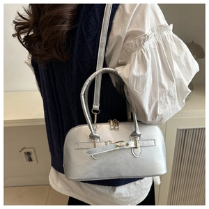 Close-up of metallic silver shell bag with gold hardware and adjustable strap on a model