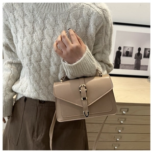 Detail of a beige crossbody square bag with a gold buckle on a white knit sweater background