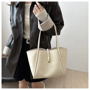 Detail of minimalist cream tote bag with gold buckle on a black leather coat