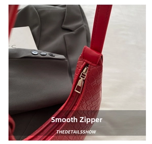 Close-up of metal zipper detail and red woven texture on crescent shoulder bag