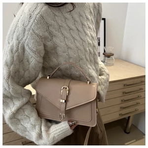 Model lifestyle shot of a beige leather crossbody bag with buckle detail and top handle