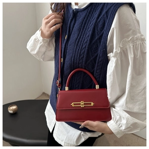 Detail of red leather crossbody bag featuring a unique gold safety pin metal clasp