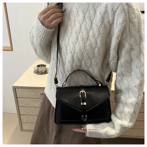 Detail of minimalist black crossbody bag with V-shaped flap and gold hardware on a model