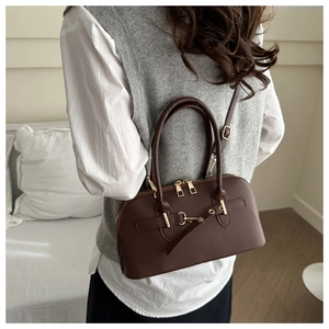 Deep brown leather bowling bag with gold hardware shown on shoulder in a home setting