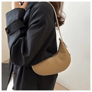 Detail of beige crescent underarm bag with crocodile pattern worn with black coat