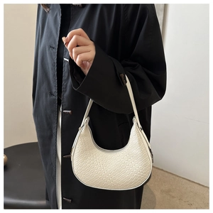 Detail of white woven crescent shoulder bag styled with a black trench coat on model