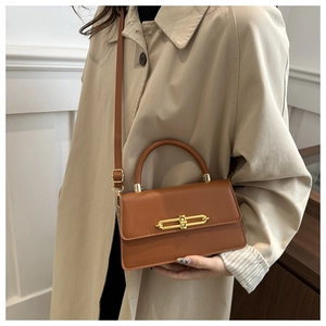 Close-up of brown leather handbag with gold bar lock and adjustable crossbody strap