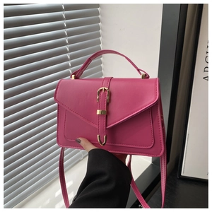 Detail of fuchsia leather handbag with gold horseshoe buckle on a white windowsill