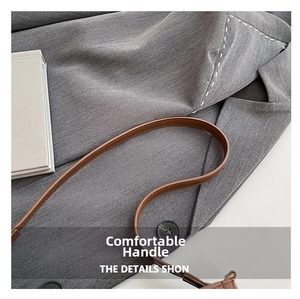 Gros plan sur la poignée en cuir marron d'un sac demi-lune chic devant un blazer gris