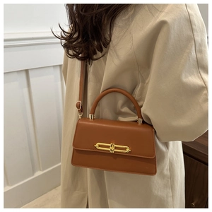 Close-up of caramel brown handbag with golden metal lock and chic top handle detail