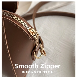 Detailed close-up of smooth golden metal zipper and brown leather texture on a shoulder bag