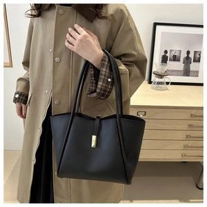 Detail of a black leather tote bag featuring a golden rectangular clasp and long straps