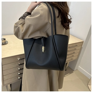 Detail view of black faux leather tote bag with gold buckle on shoulder of a model