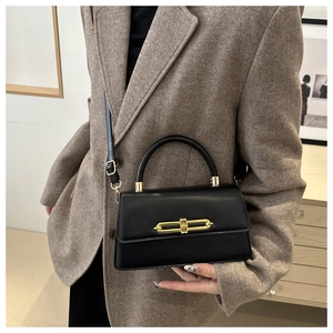 Detail of a black leather crossbody bag with gold metal buckle on a winter coat