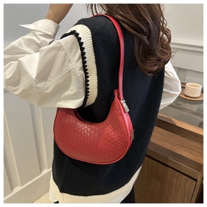 Macro shot of red woven crescent underarm bag with silver buckle and textured detail