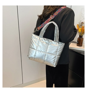 Détail d'un sac argenté matelassé avec une large bandoulière aux motifs ethniques