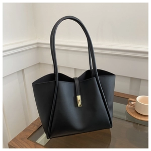 Detail of a black faux leather tote bag with gold metal buckle on a glass wooden table