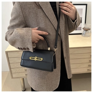 Detail of black leather flap bag with gold lock worn cross-body on a blazer