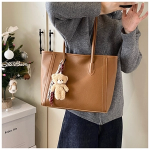 Dettaglio borsa tote marrone motivo litchi con ciondolo orsetto e foulard a righe decorativo