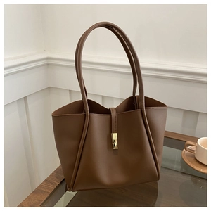 Detail view of a vintage brown leather tote bag with gold buckle on a stylish wooden table