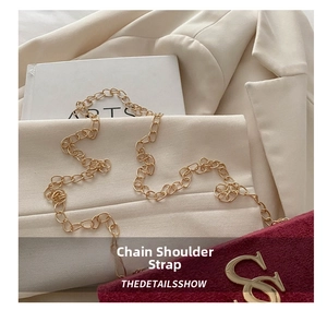 Detail of elegant gold chain strap on red suede bag against a stylish blazer
