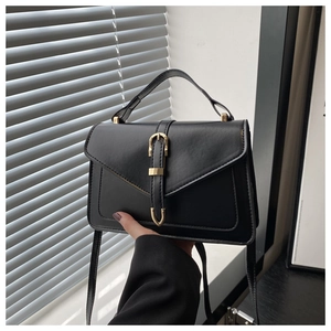 Close-up of black crossbody bag with gold buckle detail and clear faux leather texture