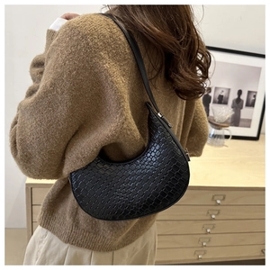 Detail of black woven hobo bag with crescent shape and silver buckle on female shoulder