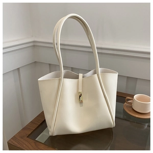 Detail view of cream tote bag with elegant gold buckle on a stylish wooden table