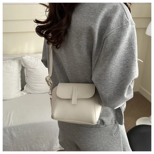 Detail of a creamy white shell bag with a minimalist flap and vertical strap detail