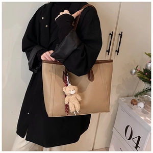 Close-up of khaki tote bag with contrast brown trim and cute plush bear accessory
