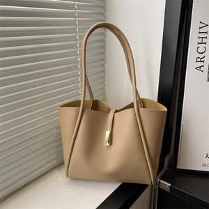 Minimalist beige tote bag with gold metal buckle and slender shoulder straps in soft lighting