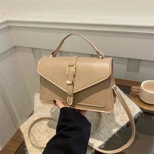 Nude beige minimalist square handbag with gold buckle held in a cozy indoor setting