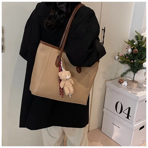 Detail of khaki leather tote bag with dark brown straps and a cute plush bear charm
