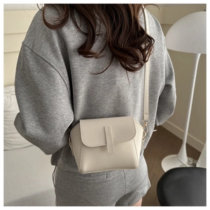 Minimalist beige crossbody square bag with gold hardware worn by model in home setting