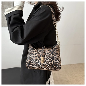Close-up of leopard print baguette bag with gold chain strap worn over a black blazer