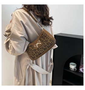 Détail du sac léopard sous le bras avec bandoulières en cuir marron et nœud doré