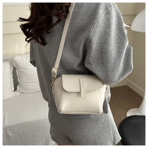 Close-up of minimalist white leather crossbody bag worn by model in casual grey outfit