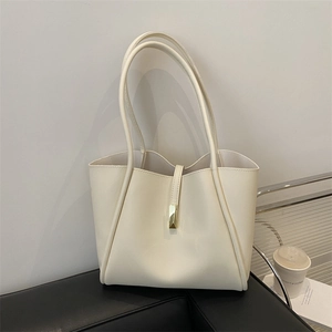 Minimalist beige leather tote bag with gold buckle and spacious interior on a sofa